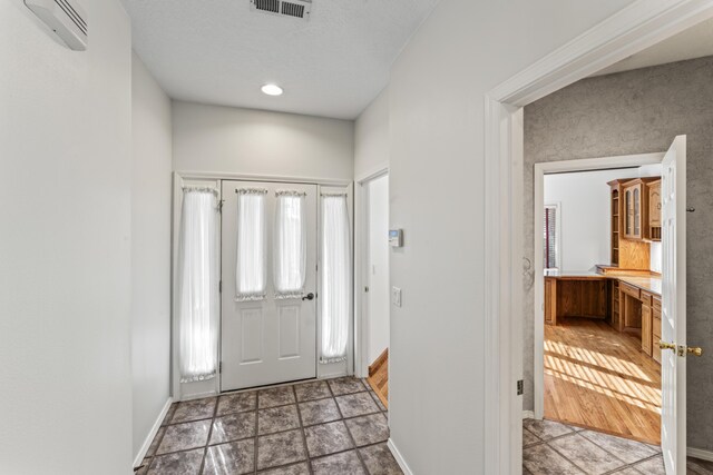 foyer entrance with a wall unit AC, baseboards, and visible vents