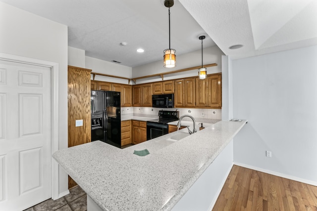 kitchen with hanging light fixtures, brown cabinetry, a sink, a peninsula, and black appliances