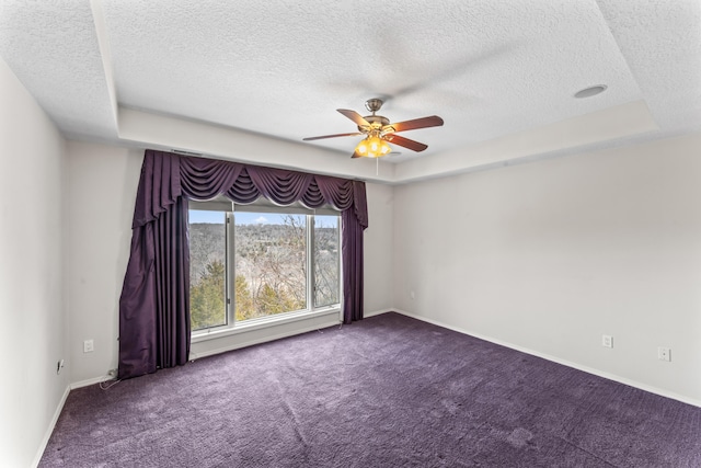 carpeted empty room featuring a ceiling fan, a tray ceiling, a textured ceiling, and baseboards