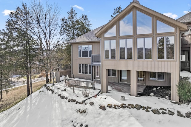 snow covered back of property with a garage, a shingled roof, a sunroom, and a deck