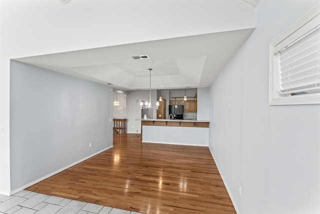 unfurnished living room with wood finished floors, a raised ceiling, visible vents, and baseboards