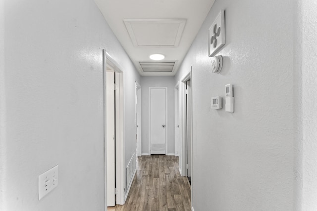 hallway with visible vents, wood finished floors, attic access, and baseboards