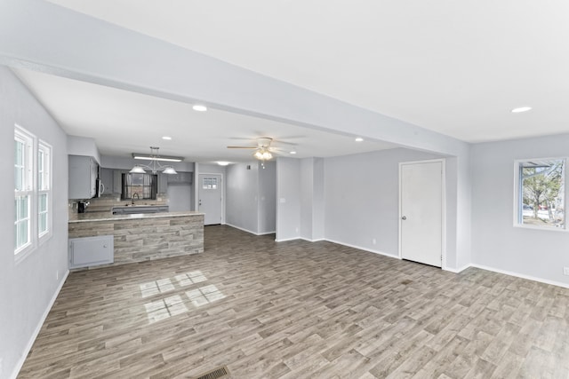 unfurnished living room with recessed lighting, baseboards, light wood-type flooring, a sink, and ceiling fan with notable chandelier