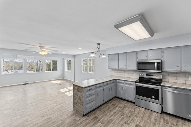 kitchen featuring gray cabinetry, stainless steel appliances, a peninsula, light wood-style floors, and decorative backsplash