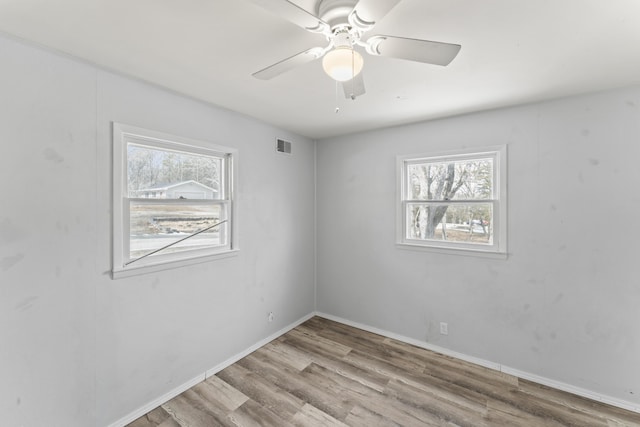 unfurnished room with a healthy amount of sunlight, baseboards, visible vents, and wood finished floors