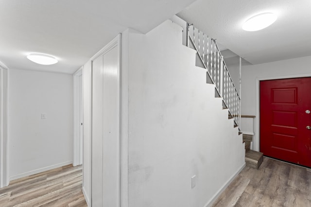 entrance foyer with a textured ceiling, stairs, baseboards, and wood finished floors