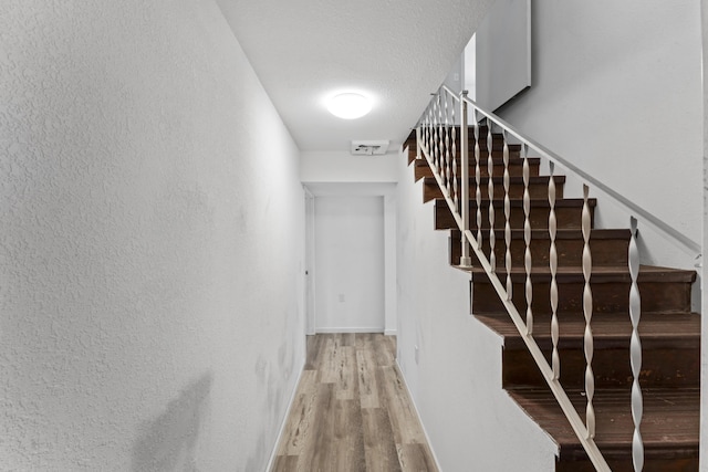 stairway with a textured ceiling, baseboards, wood finished floors, and a textured wall