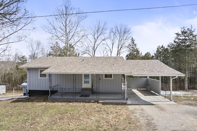 view of front of property featuring dirt driveway, an attached carport, roof with shingles, and board and batten siding