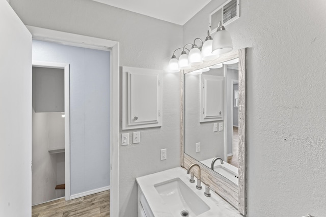 bathroom featuring a textured wall, vanity, wood finished floors, and visible vents