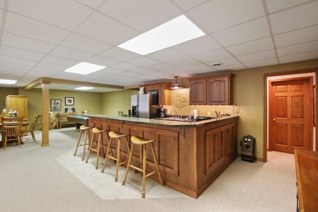 kitchen with a paneled ceiling, a peninsula, a breakfast bar, stainless steel refrigerator with ice dispenser, and brown cabinetry