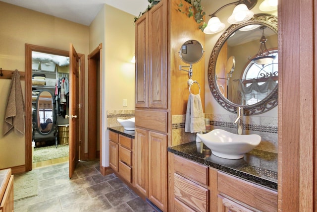 full bathroom featuring stone finish floor, a walk in closet, and vanity