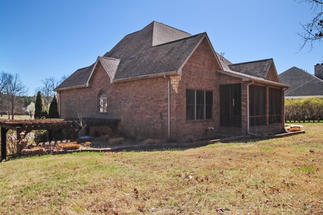 view of side of property featuring a yard, brick siding, a shingled roof, and a sunroom