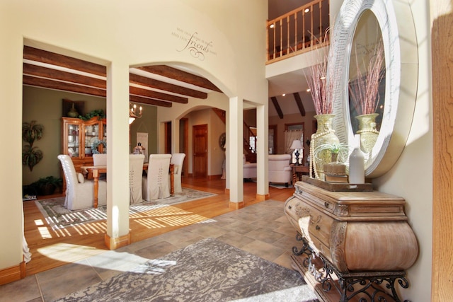 entrance foyer featuring a chandelier, a high ceiling, beamed ceiling, and arched walkways