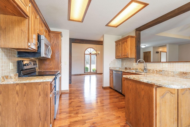 kitchen with brown cabinets, a peninsula, stainless steel appliances, light wood-style floors, and a sink