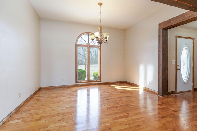 empty room featuring baseboards, an inviting chandelier, and light wood-style floors