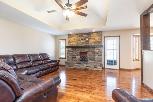 living room with light wood-style flooring, a tray ceiling, ceiling fan, and baseboards