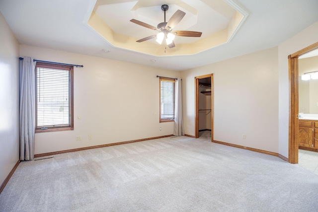 unfurnished room featuring a ceiling fan, a raised ceiling, light colored carpet, and baseboards