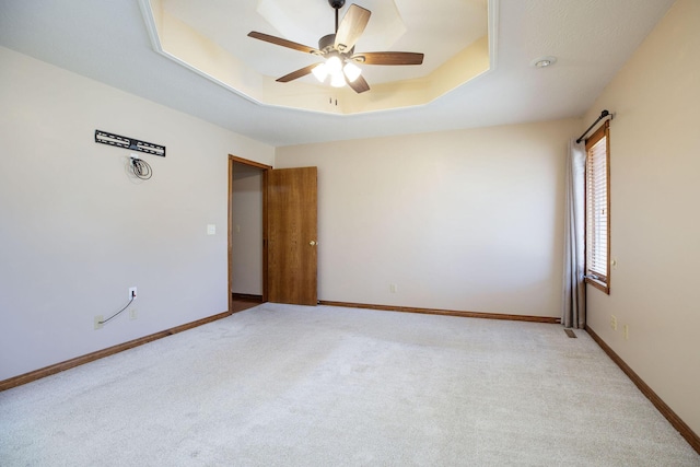 unfurnished room featuring light carpet, baseboards, a tray ceiling, and ceiling fan