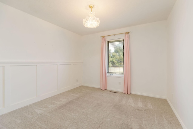 empty room featuring light carpet, a chandelier, visible vents, and a decorative wall