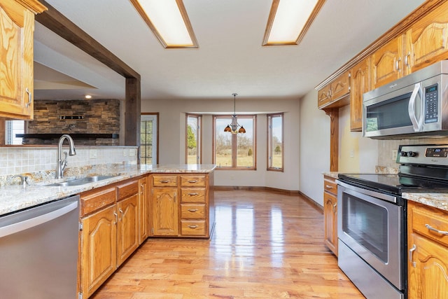 kitchen featuring tasteful backsplash, appliances with stainless steel finishes, light wood-style floors, a sink, and light stone countertops