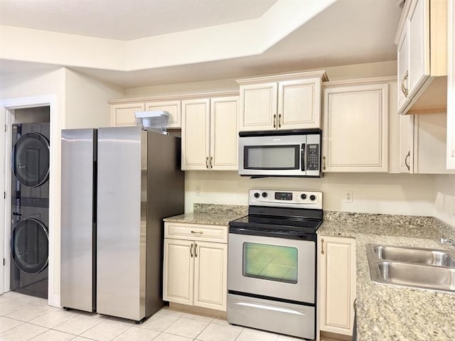 kitchen with light tile patterned flooring, stacked washer / dryer, a sink, appliances with stainless steel finishes, and cream cabinetry