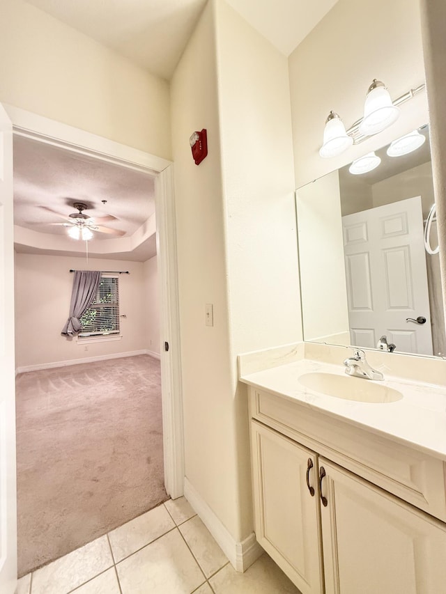 bathroom with baseboards, a raised ceiling, a ceiling fan, tile patterned flooring, and vanity