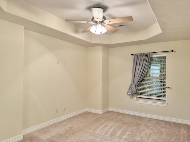 empty room with baseboards, ceiling fan, a tray ceiling, and light colored carpet