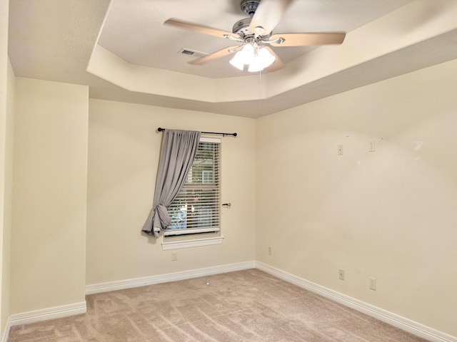 unfurnished room featuring a tray ceiling, light colored carpet, ceiling fan, and baseboards