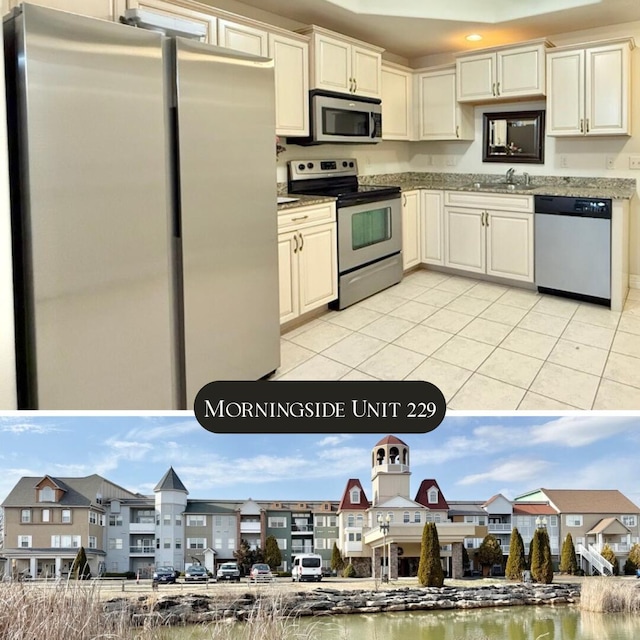 kitchen with appliances with stainless steel finishes, a sink, light stone counters, and light tile patterned floors