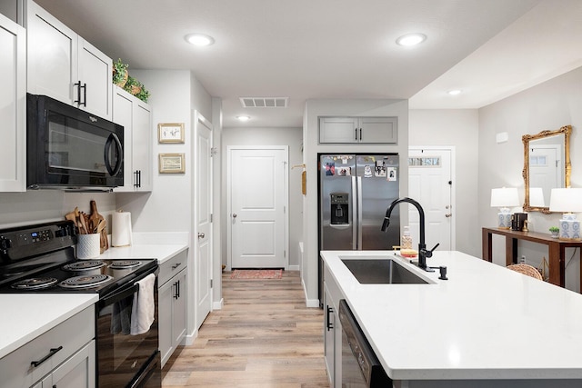 kitchen featuring a kitchen island with sink, a sink, visible vents, black appliances, and light wood finished floors