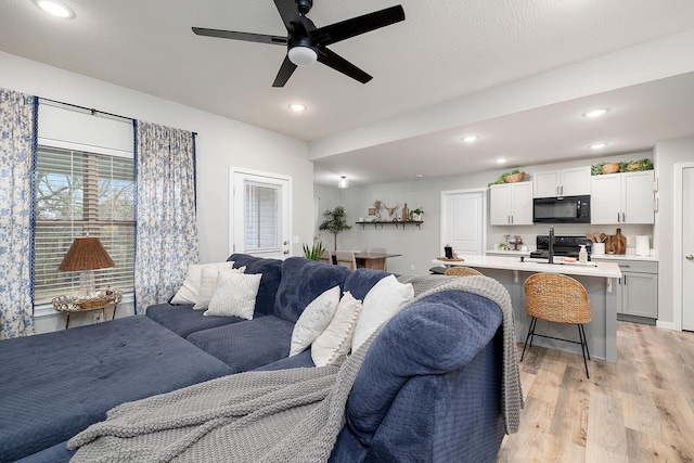 living room with light wood-type flooring, a ceiling fan, and recessed lighting