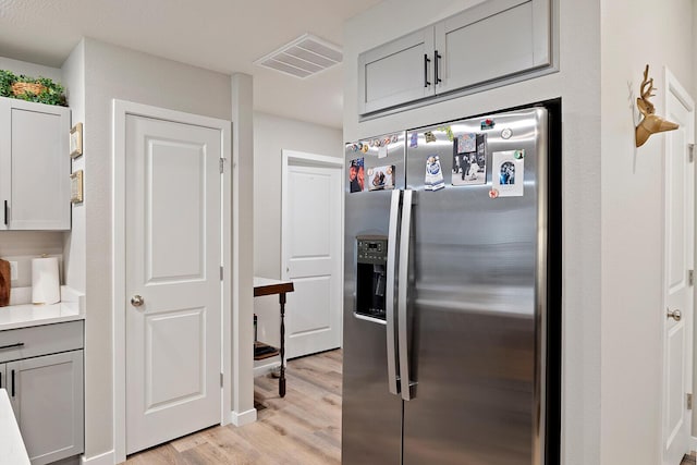 kitchen with stainless steel fridge, visible vents, light wood-style flooring, light countertops, and gray cabinetry