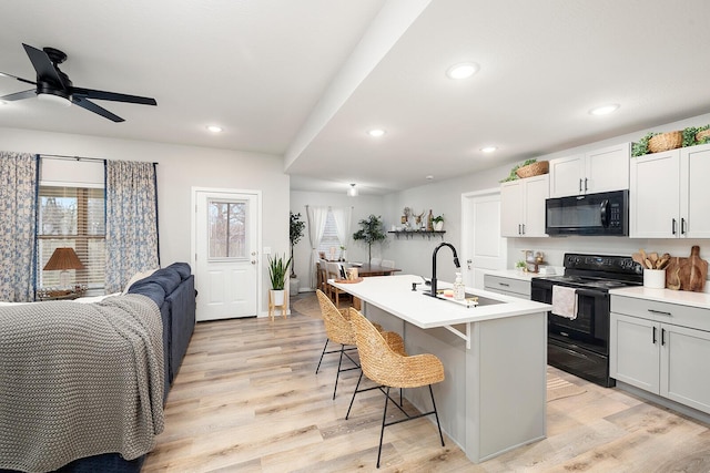 kitchen with light wood finished floors, open floor plan, a kitchen breakfast bar, black appliances, and a sink