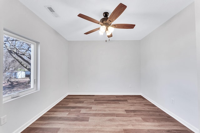 empty room with a ceiling fan, wood finished floors, visible vents, and baseboards