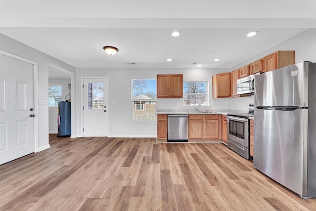 kitchen with stainless steel appliances, light countertops, water heater, a sink, and light wood-type flooring