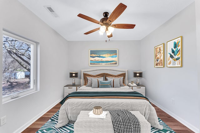 bedroom with a ceiling fan, wood finished floors, visible vents, and baseboards