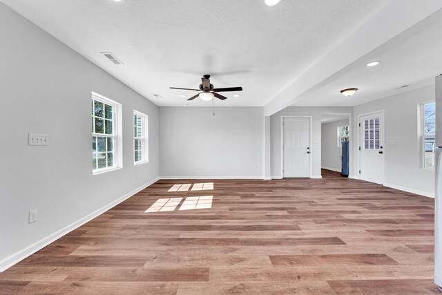 spare room with baseboards, light wood-type flooring, visible vents, and a healthy amount of sunlight