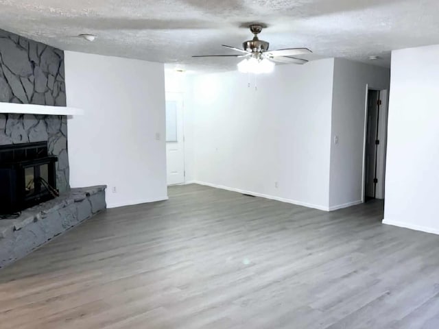 unfurnished living room featuring a textured ceiling, a stone fireplace, wood finished floors, and baseboards