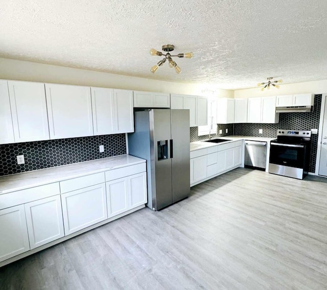 kitchen featuring light wood finished floors, appliances with stainless steel finishes, decorative backsplash, and under cabinet range hood