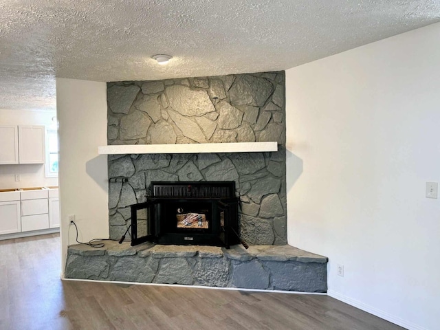 details featuring baseboards, a stone fireplace, a textured ceiling, and wood finished floors