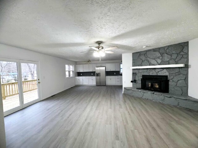 unfurnished living room with a textured ceiling, a stone fireplace, a ceiling fan, and light wood-style floors