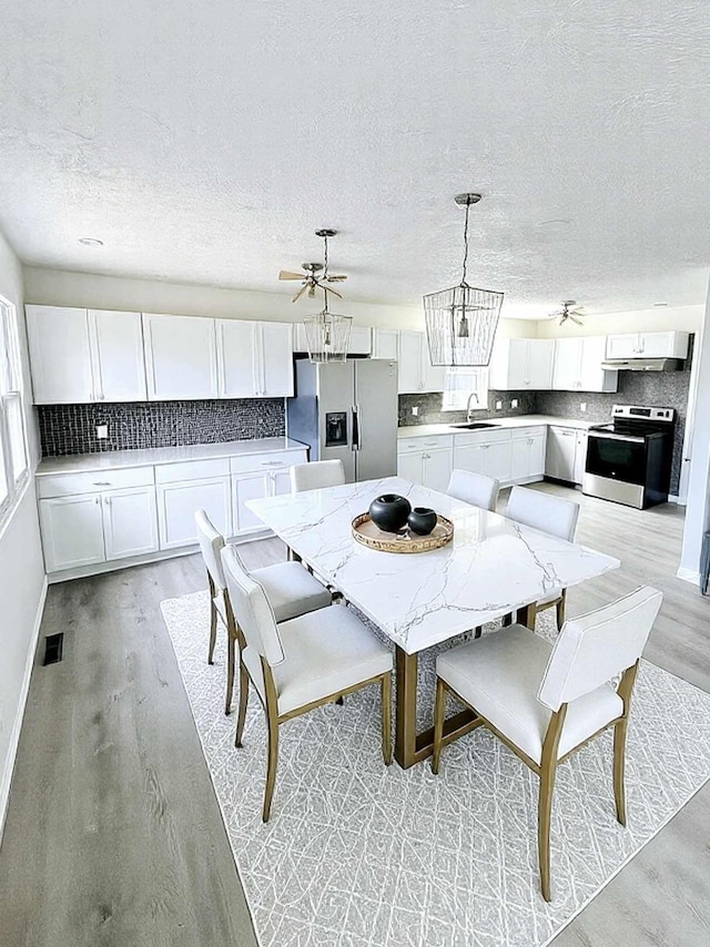 dining space featuring baseboards, visible vents, a textured ceiling, light wood-style floors, and ceiling fan with notable chandelier