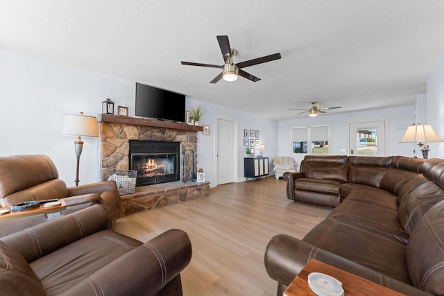 living room with a ceiling fan, a fireplace, a textured ceiling, and wood finished floors