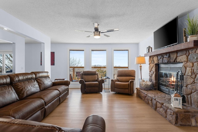 living area with a wealth of natural light, wood finished floors, and a stone fireplace