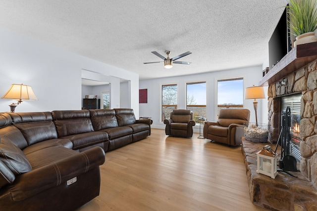 living area with a textured ceiling, a stone fireplace, wood finished floors, and a ceiling fan