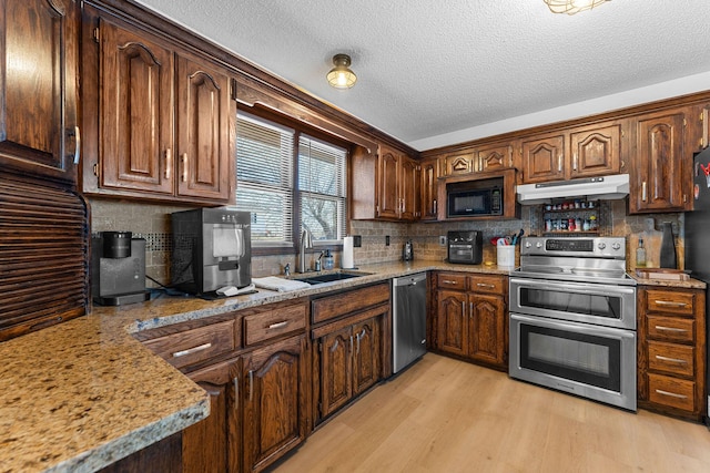 kitchen featuring decorative backsplash, light wood-style flooring, stainless steel appliances, under cabinet range hood, and a sink