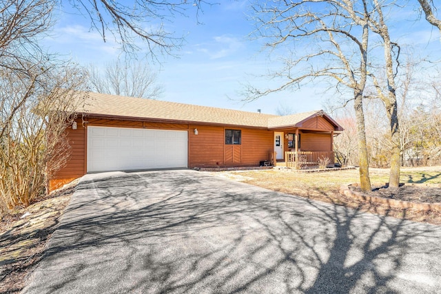 ranch-style home featuring aphalt driveway, covered porch, and an attached garage