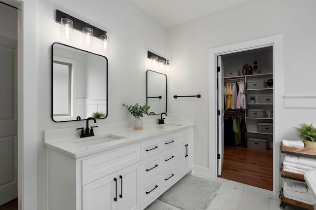 full bath with a walk in closet, marble finish floor, a sink, and double vanity