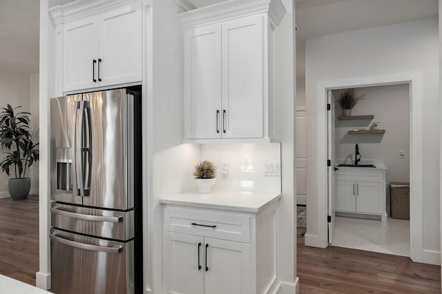 kitchen featuring a sink, wood finished floors, stainless steel fridge, and white cabinetry