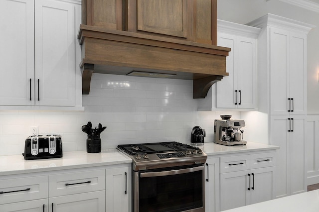 kitchen featuring stainless steel range with gas cooktop, light countertops, backsplash, white cabinets, and premium range hood